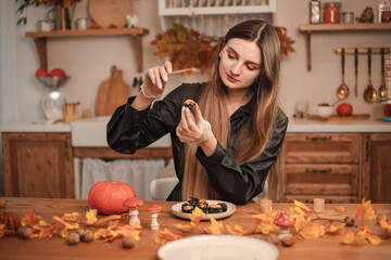 Woman confectioner decorates candy in the form of black skulls for Halloween with gold. The process of creating candies for Halloween