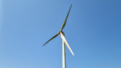close view of wind turbine with three blades and clear blue sky in background