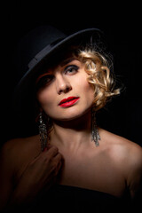 Sexy fashionable woman in an elegant hat and black dress. Mysterious blonde in retro style on a black.
