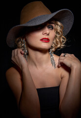 Fototapeta na wymiar Sexy fashionable woman in an elegant hat and black dress. Mysterious blonde in retro style on a black.