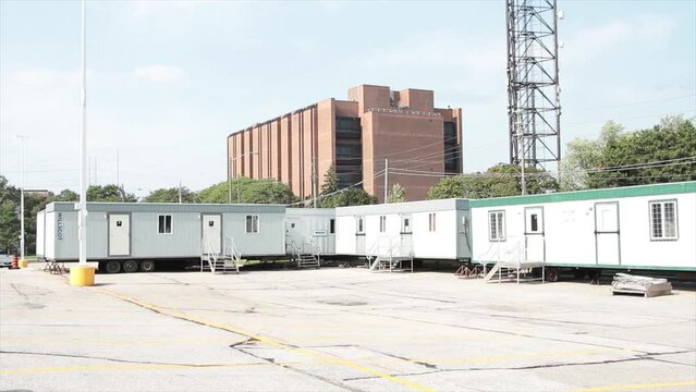 portable work trailers offices buildings containers parked in parking lot with doors and stairs with cars vehicles traffic passing on road street in background