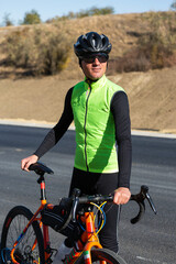 Cyclist riding bicycle on road against clear sky. A man in an outfit stands with a bicycle on an autumn sunny day.