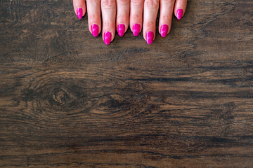 Detail of the fingers of a young girl's hand, joined together on a wooden table. High contrast between feminine purple nail polish and the wood background with various grains.