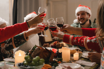 Closeup of group of people toasting with wine glasses at festive dinner table celebrating...