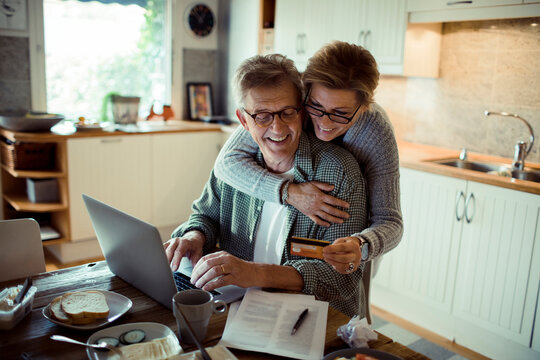 A joyful senior couple shares a moment while making an online purchase at home