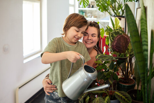 A joyful young woman and a child share a bonding moment while watering indoor plants