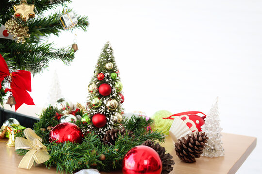 Small decorating Christmas tree with fir garland, ball pine cone and beautiful ornament items on wooden desk in white living room. Preparation for happy celebrating winter holiday. Merry Christmas