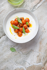 Bowl of tirokafteri or greek feta dip sauce with roasted tomatoes, vertical shot on a grey granite background, above view