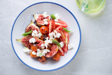 Salad with tomatoes, fresh figs and goat cheese served in a blue and white plate, flat lay on a light-grey granite background