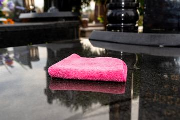 Cleaning a black tombstone with a cloth and water at a cemetery in Poland, visible pink cloth.
