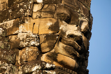 A huge face carved in stone, cut out against the blue sky, at Bayon temple, Angkor, Cambodia.