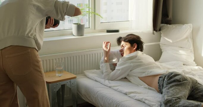 backstage of photo shoot, young photographers with professional equipment takes pictures a sexy man who is lying on a bed, hugging pillow Slow motion