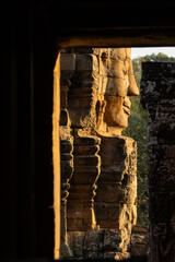 A huge face sculpted in stone, framed by the opening of a passageway, looks out into the afternoon light at Bayon temple, Angkor, Cambodia.