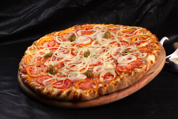 Pizza on a black background with kitchen utensils and ingredients around it, in a studio shot with a black background
