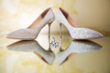 Sparkling bridal heels reflect a mirrored image, emphasizing their glitter design. Between them,...