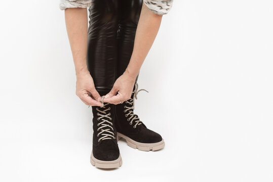 A woman in leather black pants tries on high black boots on aggressive sole on a light background, ties the shoelaces, gets used to new shoes