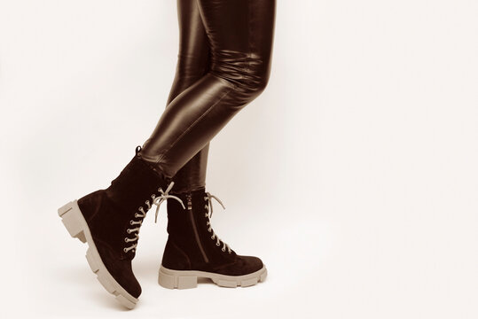 A woman in leather black pants tries on high black suede boots with a high aggressive sole on a light background, chooses practical warm shoes for every day
