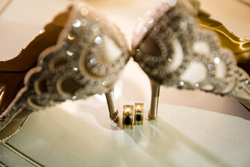 Close-up of champagne heels with lace patterns and crystals, paired with detailed gold wedding...