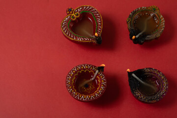 Happy Diwali and Kartika Deepam Festival Greetings - Clay diya oil lamps lit in celebration of Hindu festival of lights Diwali and Kartika Deepa on red background.