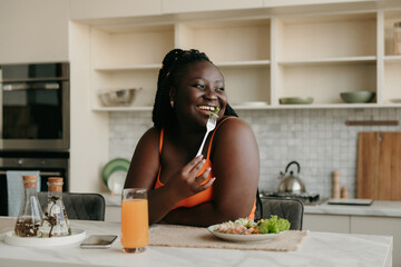 Beautiful curvy African woman enjoying healthy food for lunch at the domestic kitchen - 669206393