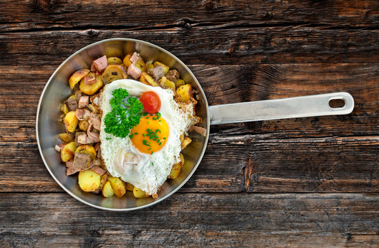 Traditional Austrian Gröstl dish in pot with fried egg on top on a rustic wooden table