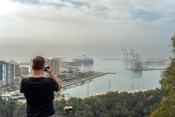 Málaga, Gibralfaro viewpoint, panoramic view of the city, man taking photos with his mobile phone from the viewpoint, views of the city's port - obrazy, fototapety, plakaty