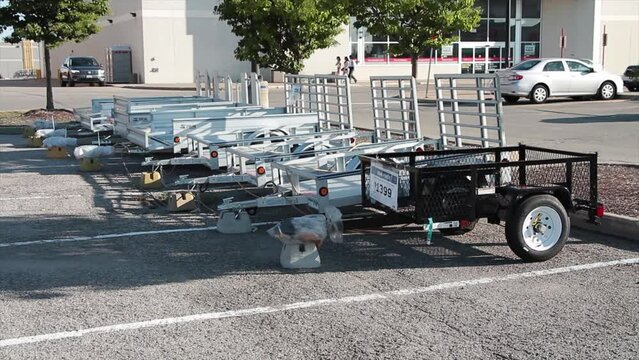 line row of two wheel welder wagon utility trailers outside outdoors on display for sale in parking lot in front of store with people walking and cars passing