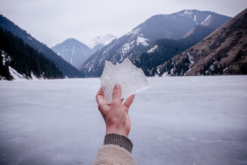 woman's hand holding a piece of ice in front of mountains and frozen lake