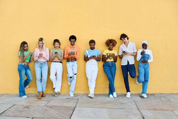 Multi-ethnic young people leaning on a wall using phone