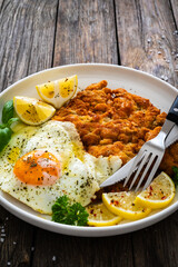 Crispy breaded seared chicken cutlet with fried egg on and  lemon on wooden table
