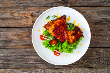 Roasted chicken thigh with lettuce and tomato on wooden table
