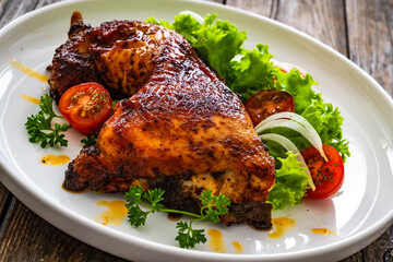 Roasted chicken thigh with lettuce and tomato on wooden table
