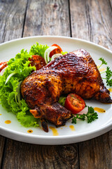 Roasted chicken thigh with lettuce and tomato on wooden table
