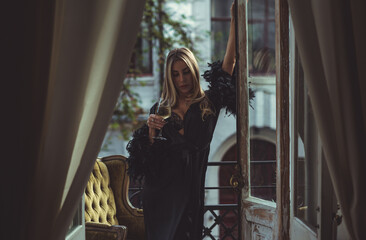 Lady in peignoir with a glass of wine. Sensual photo of European Blonde woman in black silk robe...