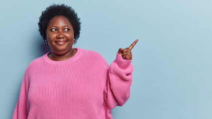 Nice offer. Dark skinned overweight woman with curly hair points finger at blank space shows...