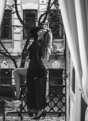 Lady in peignoir with a glass of wine. Sensual photo of European Blonde woman in black silk robe with feathers sleeve. Fashionable concept