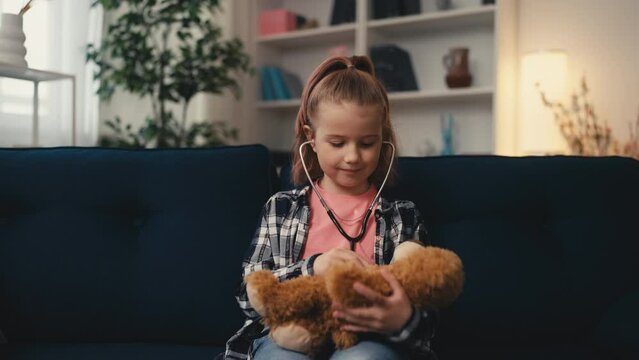 Smiling girl listening to teddy bear with stethoscope, playing a doctor, dream
