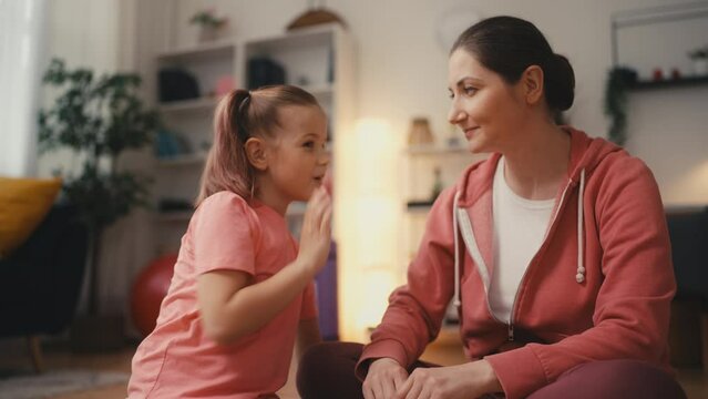 Cute little girl sharing secrets with mom during fitness break at home, trust