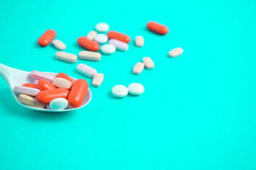 Colorful Medicine Pills in White spoon on green tosca background, supplement, vitamin, colorful