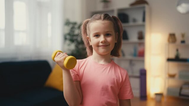 Portrait of a smiling girl lifting a dumbbell, healthy living from young age