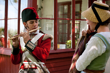 Young redcoat playing the flute for the young girl in old-fashioned dress.