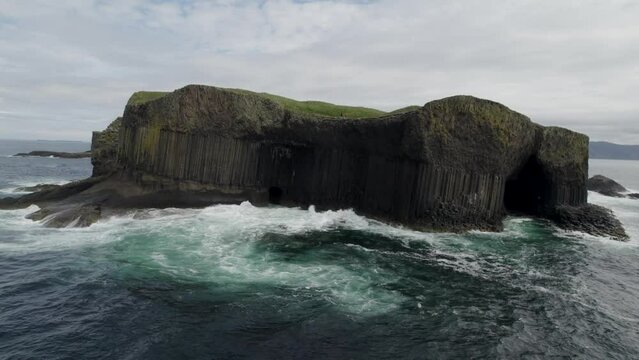 Aerial view flying over a Fingal's Cave on Staffa Island, west of Isle of Mull in Scotland. Calm waves touching the rocks. 4k video.