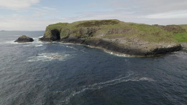 Aerial view flying over a Fingal's Cave on Staffa Island, west of Isle of Mull in Scotland. Calm waves touching the rocks.