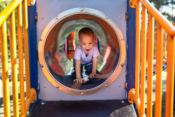 Cheerful boy crawling in play house tunnel outdoors.