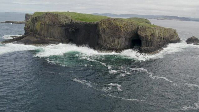 Aerial view flying over a Fingal's Cave on Staffa Island, west of Isle of Mull in Scotland. Calm waves touching the rocks.