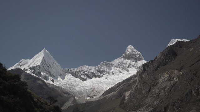 ice covered glacier of a pyramid shaped mountain at laguna paron lagoon in the high andes mountains of the cordillera blanca at huascaran, Peru, with snow covered mountain peaks on a bright sunny day.