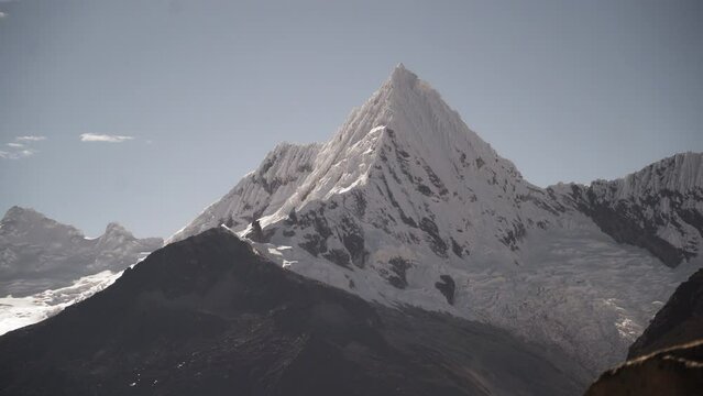 ice covered glacier of a pyramid shaped mountain at laguna paron lagoon in the high andes mountains of the cordillera blanca at huascaran, Peru, with snow covered mountain peaks on a bright sunny day.