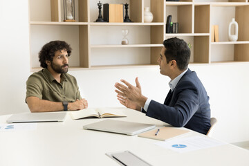 Two serious diverse business colleagues men discussing startup project, planning teamwork strategy, cooperation, talking on agreement, partnership, working together at meeting table