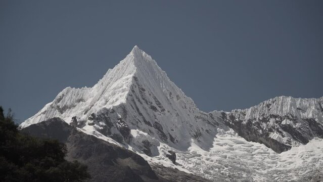 ice covered glacier of a pyramid shaped mountain at laguna paron lagoon in the high andes mountains of the cordillera blanca at huascaran, Peru, with snow covered mountain peaks on a bright sunny day.
