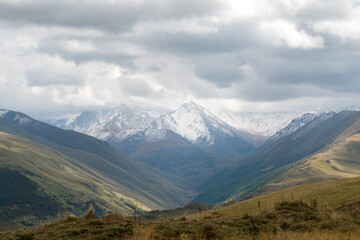 White snowy mountain peaks with low hanging clouds. Green valleys and meadows in the front